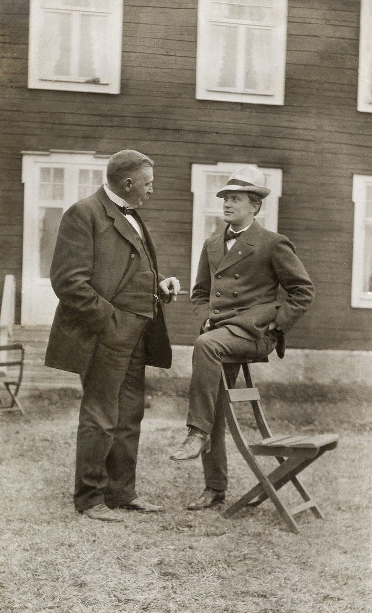 Landsfiskal Gustaf Herrlin, Åseda, samtalar med en annan man utanför en sockenstuga (?), ca 1915.
