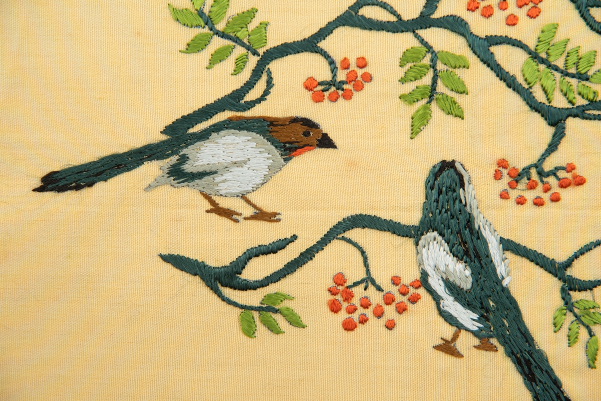 Brodert veggbilde med fuglemotiv. Tre fugler og to greiner med rognebær.