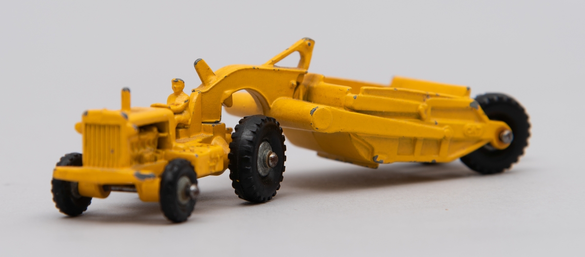 Gitt av Lisbeth Andreassen Chumak.
Traktor med henger. Begge i metall. De er gule og på traktoren sitter en mann/bonde.
