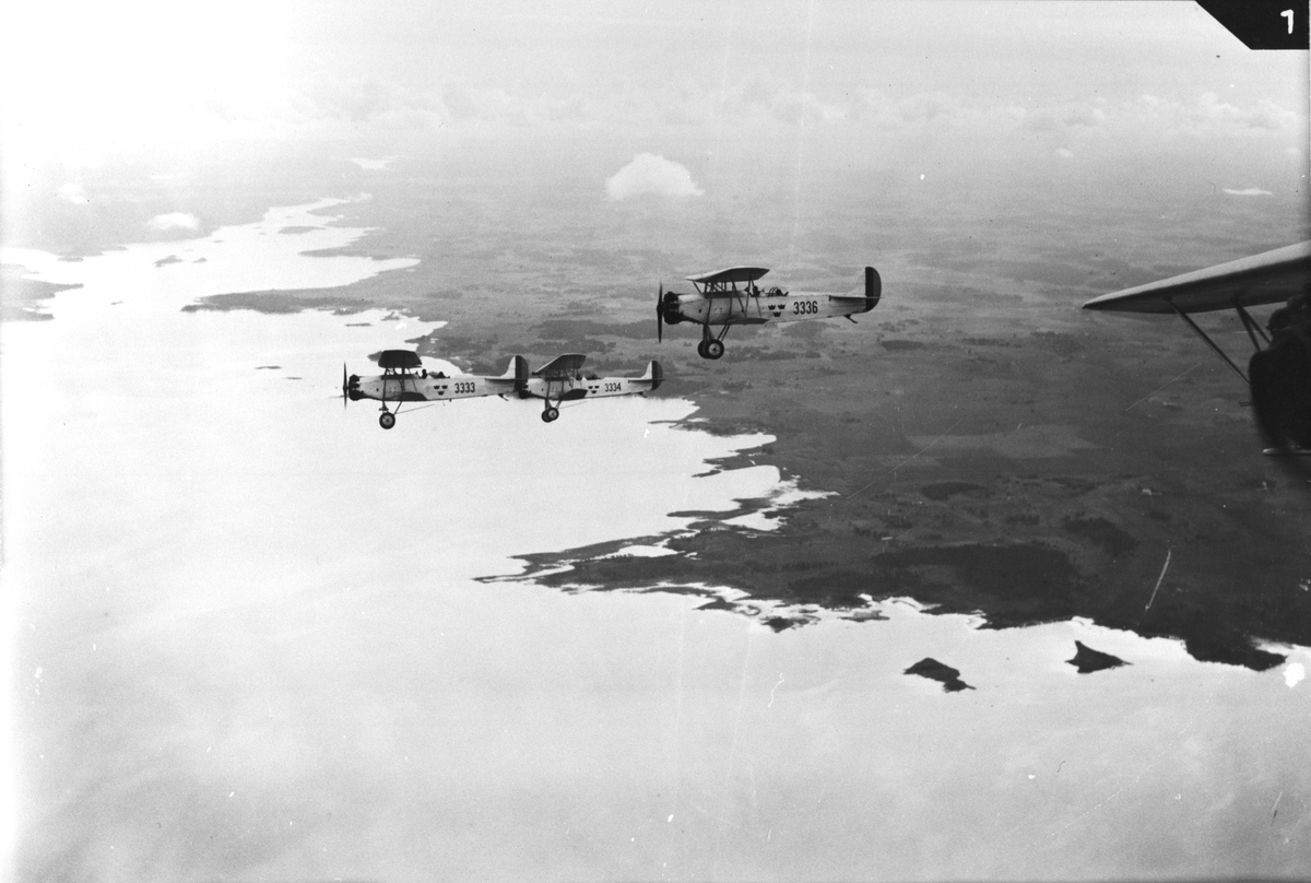 Flygfotografi av tre flygplan S 6 Fokker C.V. i formationsflygning över kustlinje. Flygplan märkt nummer 3333, 3334 samt 3336.
