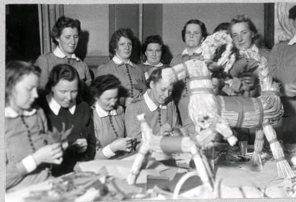 Troligen lottor som förbereder julmarknad genom halmarbeten såsom julbockar och ljusstöpning.
Tillhör samlingen med fotokopior från Hallands Nyheter som är från 1930-1940-talen.