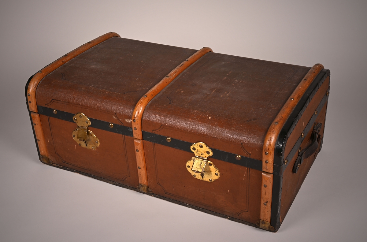 Koffert laget av tre, papp og skinn. Innsiden er kledd med papir. Den lukkes i front med to beslag. På sidene er det festet bærehåndtak av skinn.