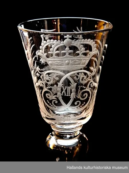 Pokal av glas med Karl XII:s krönta monogram i bladcartouche. Fot med graverad växtranka. Droppformig ihålig midja. Böhmisk typ.