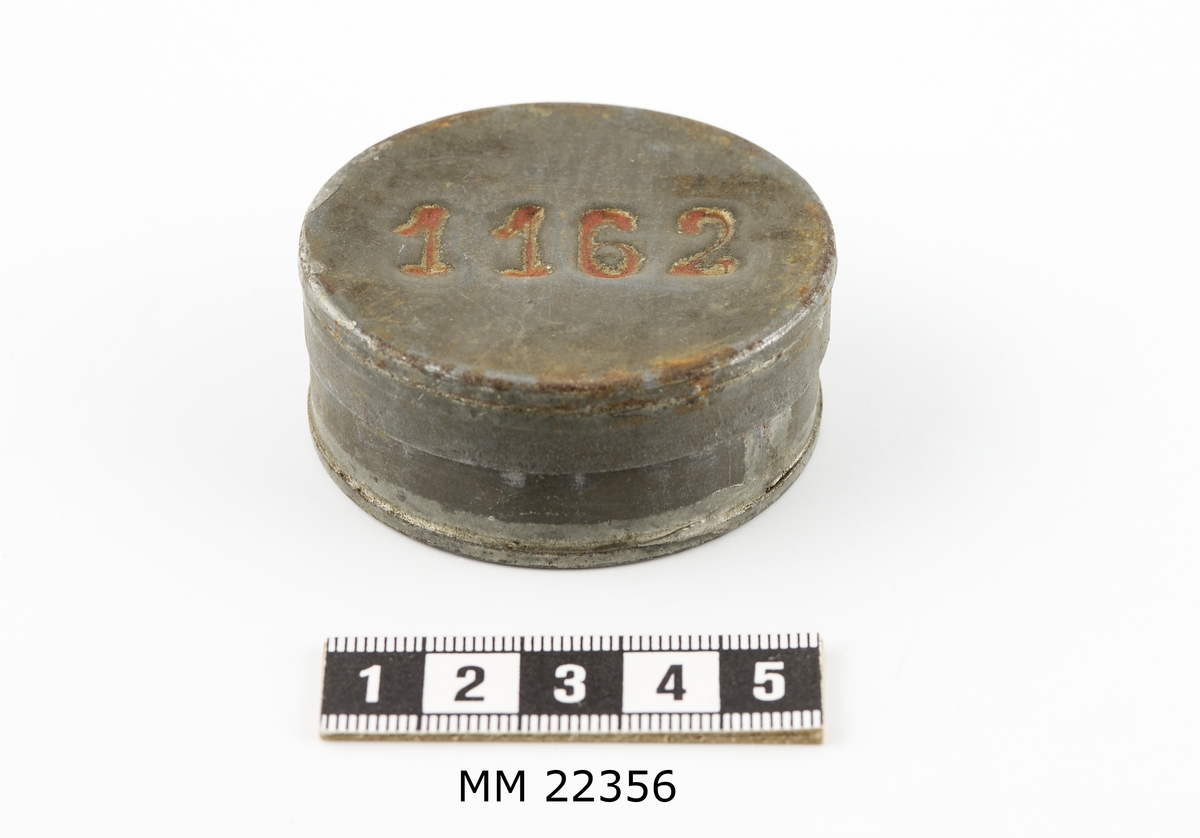 Avlöningsask av bleckplåt, rund med lock.
Märkt på locket: "1162".
Jämför K 9512.