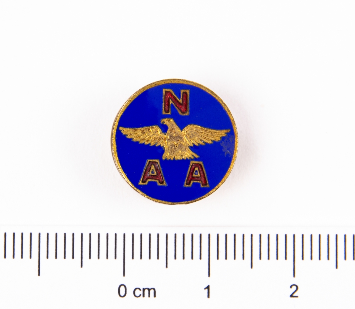 Rockslagsmärke, National Aeronautic Association, NAA. Emaljerad runt märke av mässing. I mitten en örn på blå bakgrund med röda bokstäver "NAA".