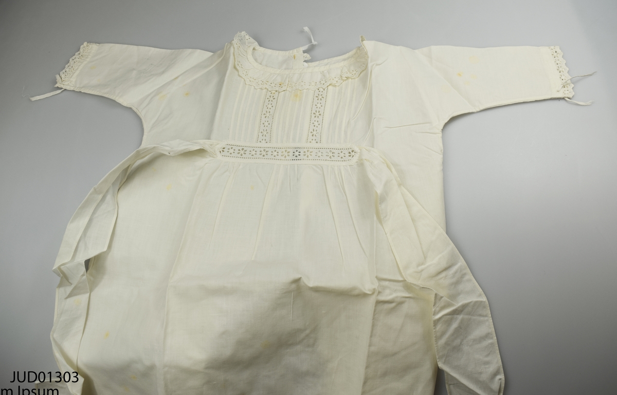 Kläder för barn i blå ask med knytband: vita, broderade klänningar, skjortor, hättor och västar, samt två par skinnhandskar i damstorlek.