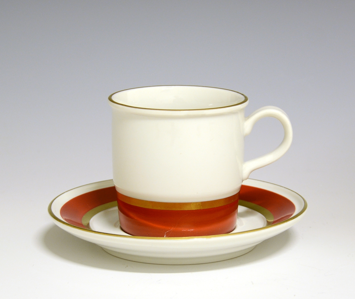 Kaffekopp av porselen. Nederst en bred rød stripe med gullbånd øver. Gullstrek på kantrand.
Modell 444/1 Eystein