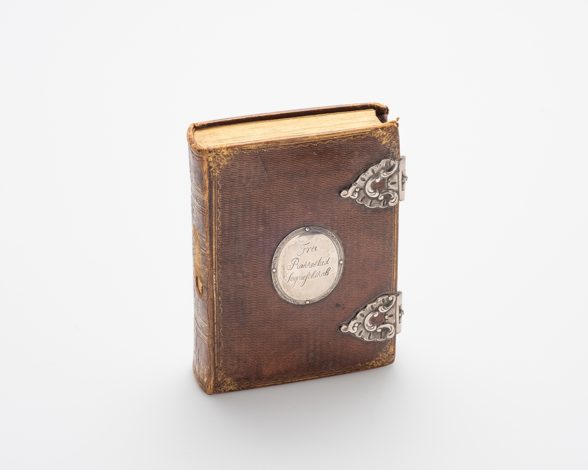Rektangulær bok, skinninnbundet med sølvbeslag.. Boken lukkes med to sølvspenner.