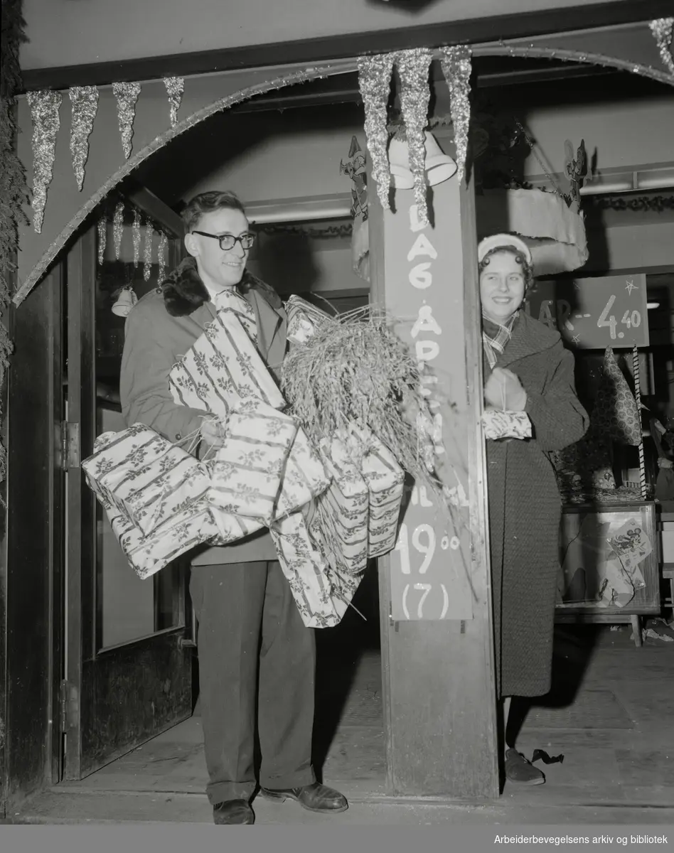 Julehandel i siste liten. Carl Fredrik Jonassen og Berith Martinsen "fanget i samme butikkdør like før stengetid." Desember 1957.