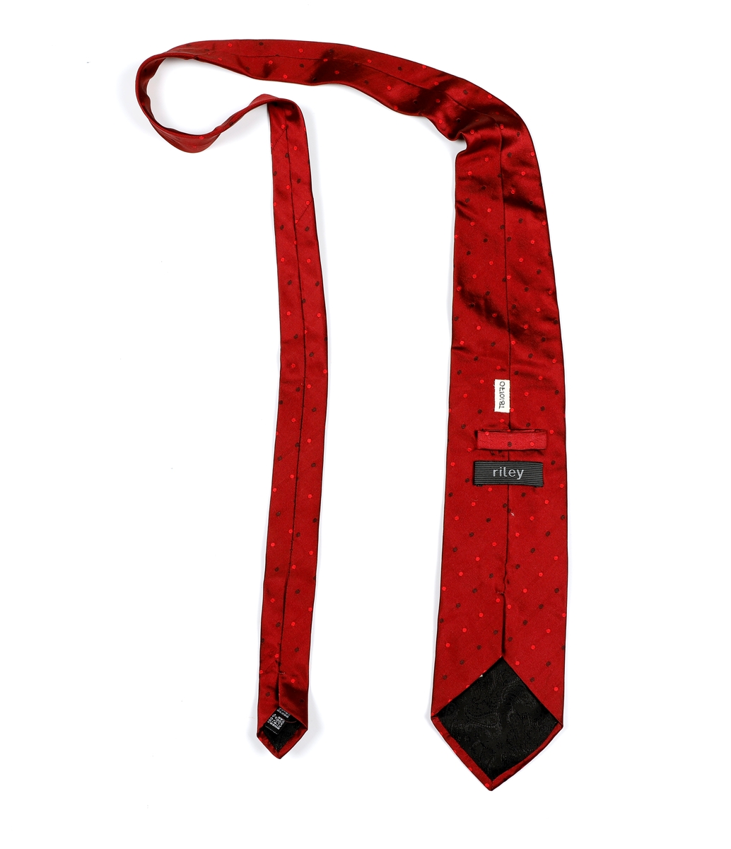 Mønstrete slips med prikker. Foret med svart stoff i paisleymønster, Sydd hempe bak til å tre den smale delen av slipset gjennom.