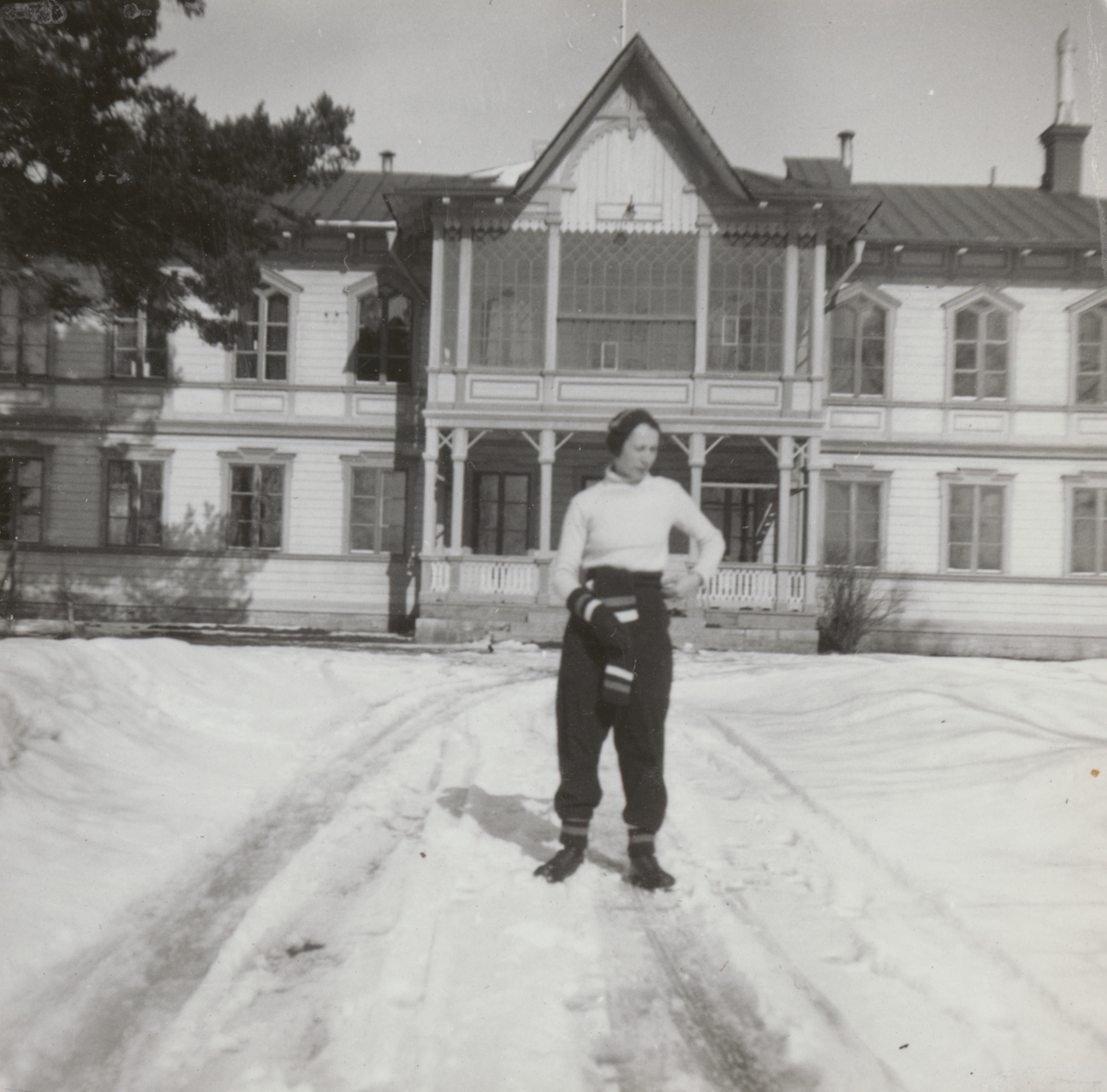 Porträttfoto av Anna Linderstam i skidklädsel utanför byggnad, vintertid, cirka 1925.

Text vid foto: "'Annika gillar 'Östran'"