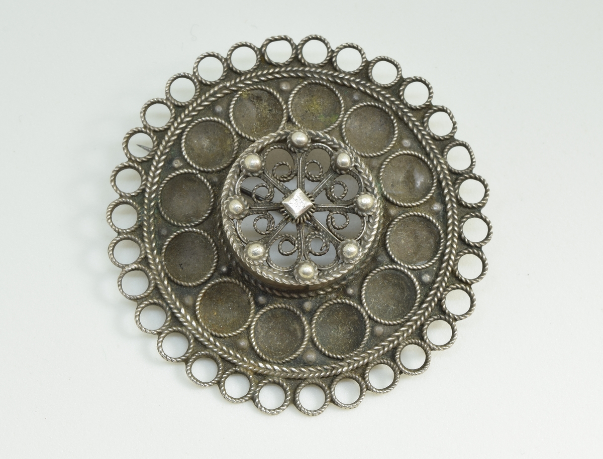 Skålesølje, 12 runde skåler omkring sylindrisk midtparti med toppen dekket av 8 filigransløkker med demant og 8 perler. Søljens rand dannet av ringer.
