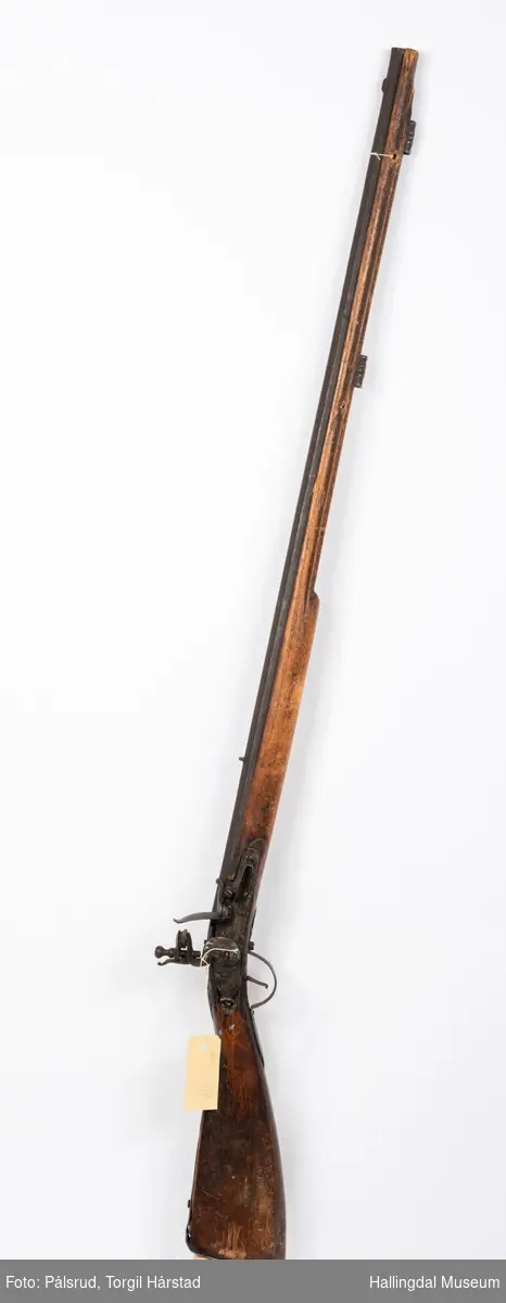 Gevær med eldre militær flintlås. Privat våpen med riflet løp. Mulig satt sammen tidlig 1800-tall.
Utskjæringer i treet bak lås. Mangler ladestokk. Ornament under lås og på kolbekappe.