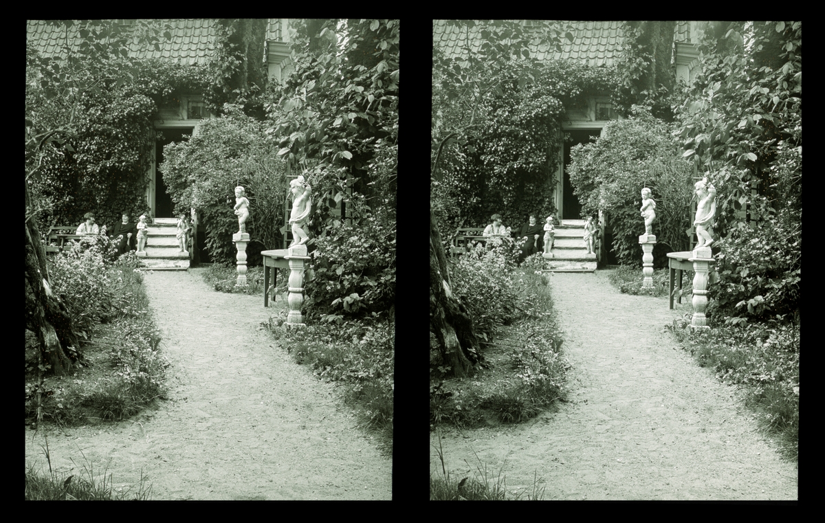 Damsgård hovedgård, viltvoksende hage med hagestatuer. To kvinner sitter i hagen. Tilhører Arkitekt Hans Grendahls samling av stereobilder.