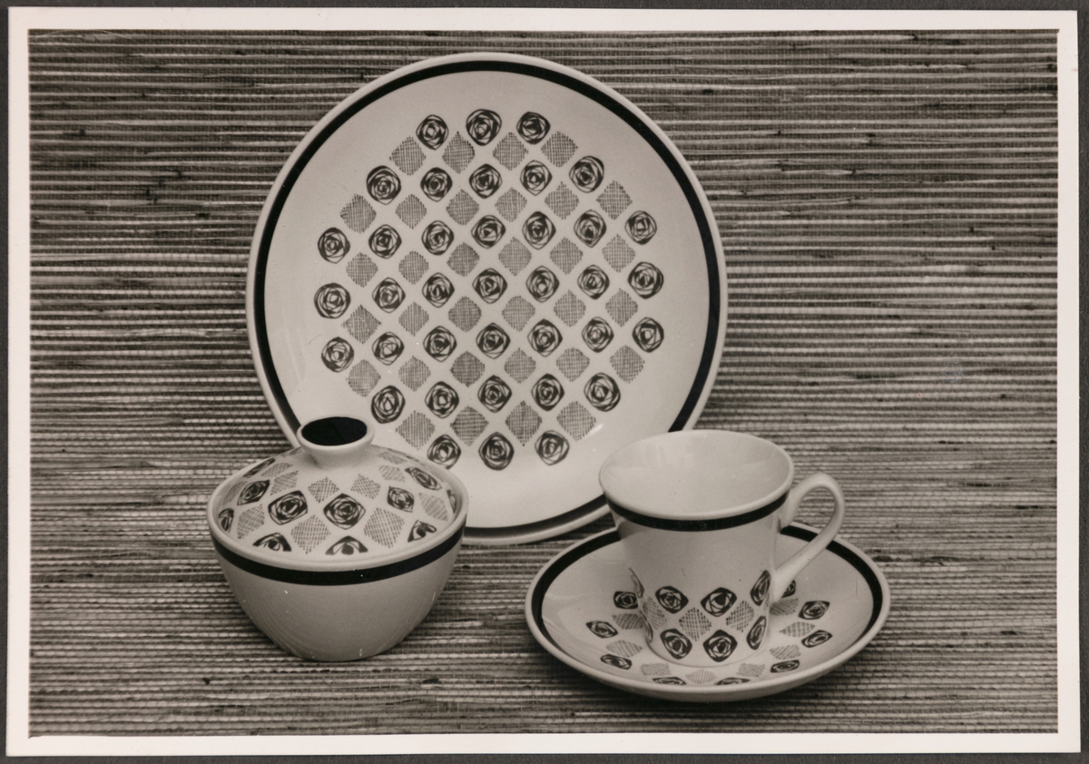 Frokostserviset "Mosaikk" fra Stavangerflint A/S. Avbildede objekter viser en tallerken, kopp med underskål, sukkerskål og bordoppdekning med kniv og gaffel. 