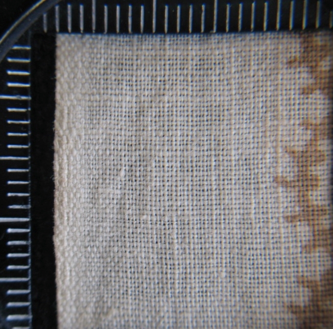 Kvadratiskt huvud- eller halskläde av vit bomullslärft med tryckt mönster. I mittspegeln regelbundet ordnade små kvistar och pickar, i bården stora blombuketter av blåklint och vallmo i orange och blå och grönanyanser, smala bårder i brunt. Smala fållar på två sidor.

/Birgitta Blixt 2019
