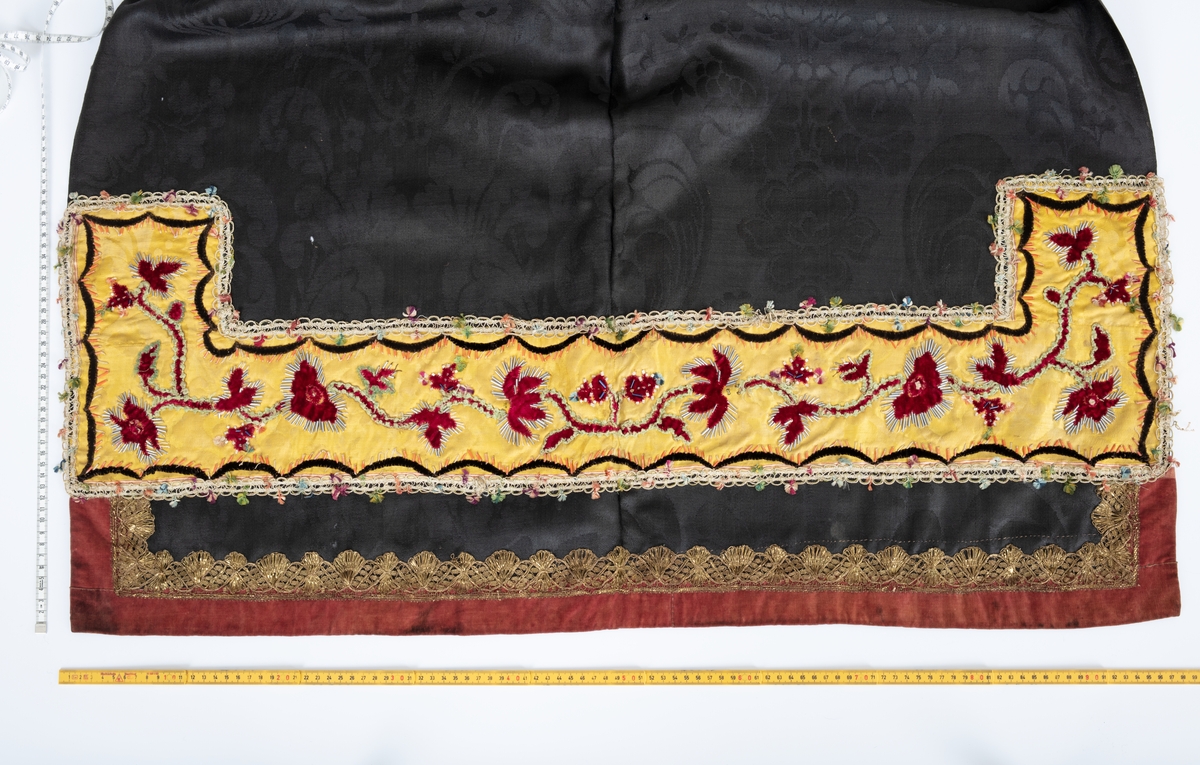 Svart forkle i ulldamask med dekor av fløyel, silkedamask, knipplet metallblonde og glassperler.