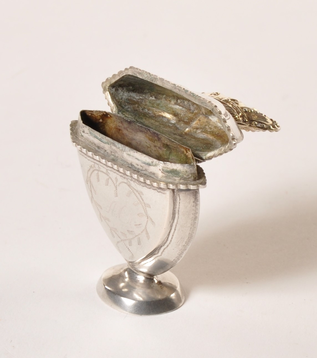Hjerteformet luktevannshus i sølv  med henglset lokk med  gullfarget krone. Stående på sokkel. Ingravert bladmønster.