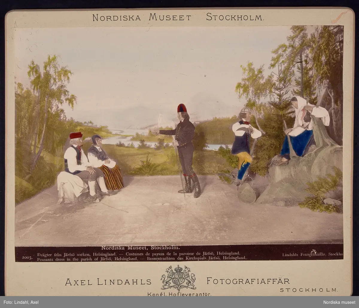 Tablå från utställningarna i Nordiska museets lokaler vid Drottninggatan. Ett arrangemang med dräkter från Bjuråker och Järvsö i  Hälsingland. Dessa kolorerade fotografier monterade på kartong såldes i museet.