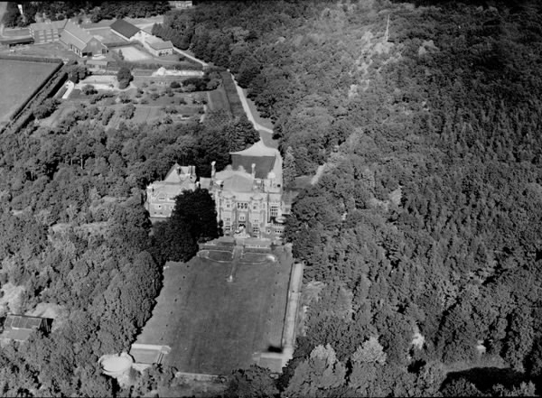 "Tjolöholms Slott, Flygfoto." Slottet sett söder ifrån med den formella trädgården i förgrunden, odlingar och ekonomibyggnader omgivet av slottsparken och de skogsklädda höjderna. I det nedre vänstra hörnet syns att kupolen på James Dicksons mausoleum är intäckt; kanske den träkåpa Dicksons använde som skydd åt den vintertid.