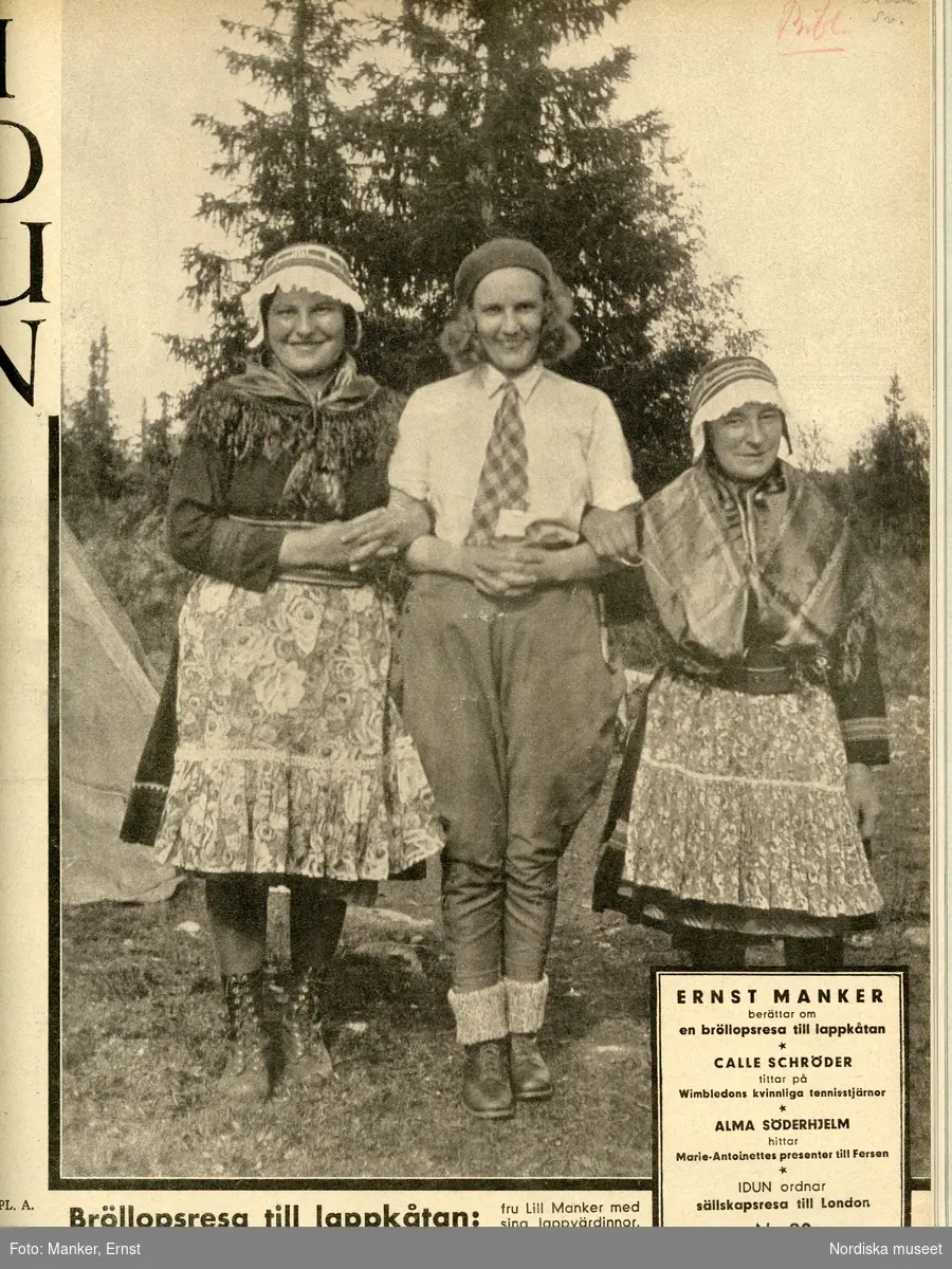 Framsida av tidningen Idun nummer 29 1934. Tre kvinnor står arm i arm, i bakgrunden landskap med granar och del av en kåta. I mitten fru Lill Manker iklädd fritidskläder, kortärmad skjorta, slips, byxor, kängor med raggsockor och på huvudet basker. De två andra kvinnorna bär samisk dräkt. Bilden är tagen i Tuolpukka under Ernst och Lill Mankers bröllopsresa till Lappland.