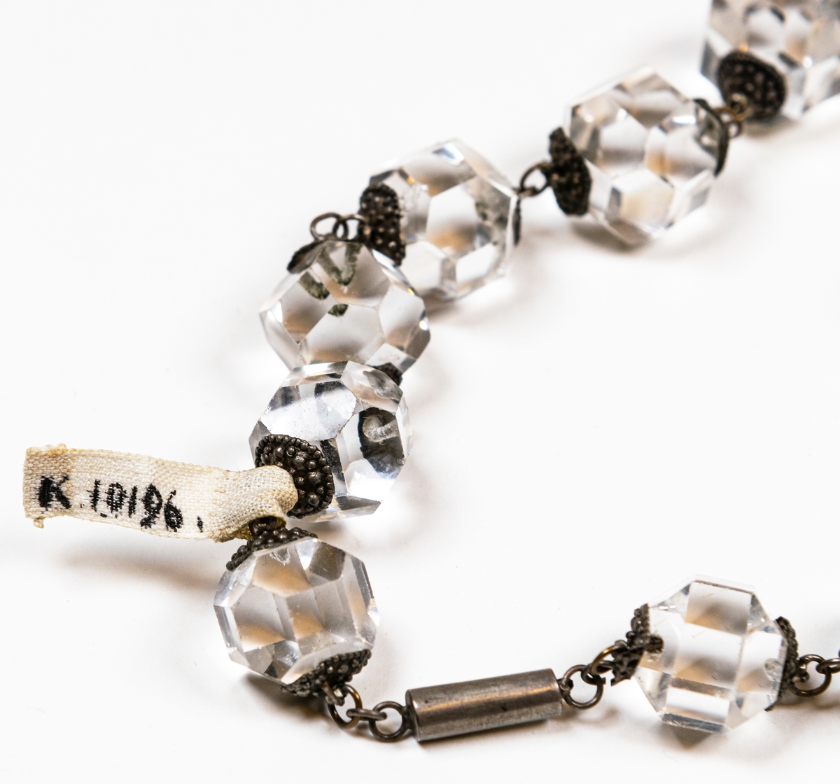 Halsband, av stora slipade glaspärlor, samt en större och fyra mindre droppformiga hängen. Pärlorna äro 19 st.