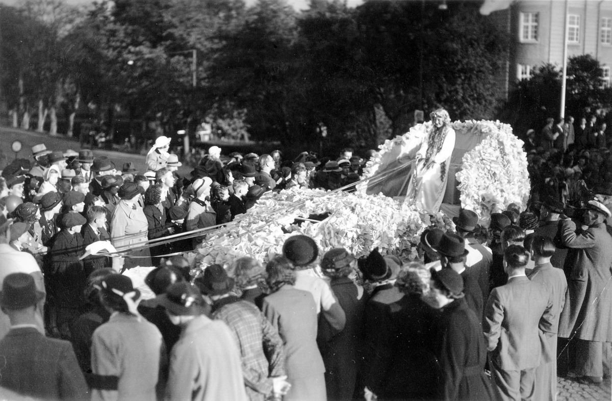 Barnens dag 1938. Blomsterflicka åker på en blombeklädd vagn i paraden förbi folksamlingen.