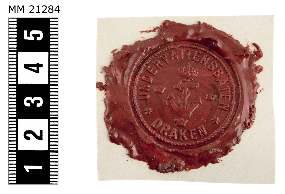 Sigillavtryck av rött lack på papper. I mitten krönt stockankare omgivet av tre kronor. Längs kanten text: "Undervattensbåten Draken".