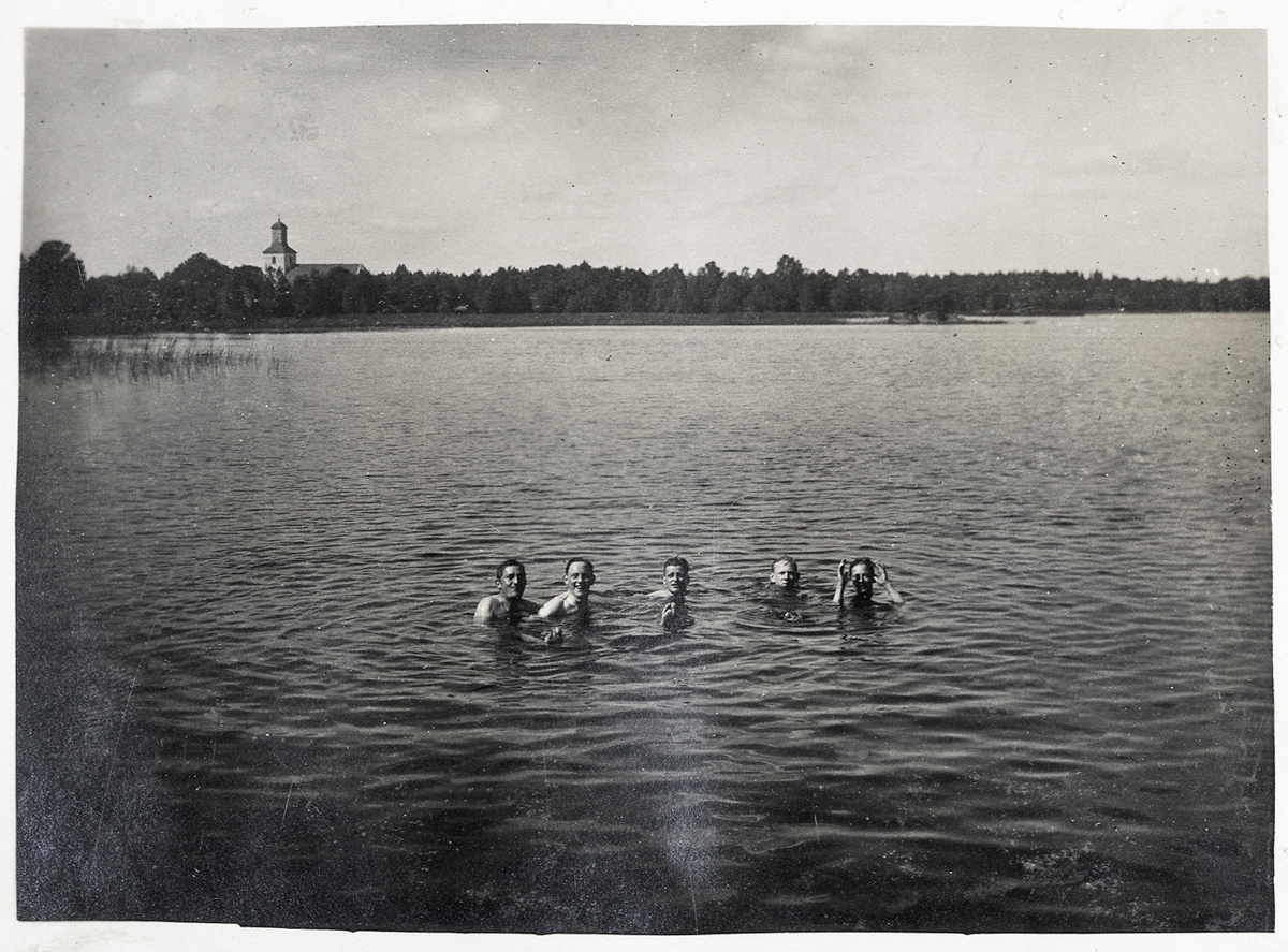 En grupp män som badar i en sjö. I bakgrunden syns bl a Almundsryds kyrka.
Vid fotot står antecknat: "Badning, sommaren 1924".