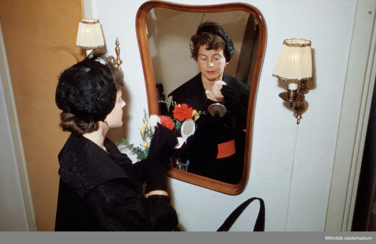 Margit pudrar näsan framför spegeln, år 1955. Hatten finns i Mölndals stadsmuseums samlingar med invnr. 03333.