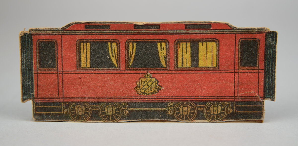 Pappersmodell föreställande röd personvagn. Tre fönster med gula gardiner. På vagnen finns skylt märkt "S.I.J.". Pappersmodellen fastlimmad på smal träpinne.