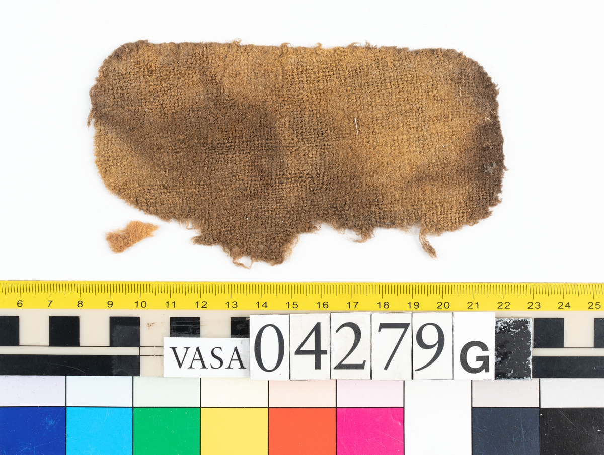 Fyndnumret är fördelat i 16 stycken askar och innehåller runt 350 stycken textilfragment av både ull och bastfiber, eventuellt lin. Tillskärning och sömmar visar att många av fragmenten varit delar av klädesplagg. Exempelvis finns delar av minst en tröja.
.
Textildokumentation 2018.
Textil, fyndnumret består av cirka 349 stycken fragment uppdelade på16 stycken askar (a-p).
Kontextgrupp 18 (inga övriga fyndnummer i gruppen).
Däck: Övre batteridäck.
Relaterade fynd: Inga.
.

Fnr 04279d Typnr 18.2:1-4 
Sammanfattning - Fyra stycken textilfragment av ull vävd i tuskaft. Färgen är nu mörkbrun, originalfärg okänd. Fragmenten är troligen delar av en dräkt.
Textilien har lugg på en sida. Luggen kommer eventuellt från färdigställningsprocessen, i så fall tillkommen genom att tyget är ruggat och överskuret (kläde).
Garnet i trs 1 är något tunnare samt hårdare spunnet än garnet i trs 2. Väven är jämn men garnet varierar något i grovlek. Fragmentens ytor är bitvis matta och har där en mer beige färg än resten av ytan. Detta beror på att den mörkbruna ytan på många av ullfibrerna är bortnött och bara den beige-gula fiberkärnan finns kvar. På ytan i textiliens lugg finns enstaka färgade fibrer.
Andra delar: Inga
Relaterade fynd: Inga.
Fragment 2:1 - Fragmentet har en kant som eventuellt är tillskuren, möjligen har den även stygnhål (söm 1).
Fragment 2:2-4 - Ingen ytterligare information.
.
Fnr 04279e Typnr 18.3:1 
Sammanfattning - Ett fragment av ull vävd i tuskaft. Färgen är nu ljusbrun/mellanbrun, originalfärg okänd. Fragmentet är troligen en del av en dräkt.
Väven är tjock och stabil och därför troligen valkad. Bindningen är bitvis svår att se pga den enhetliga ytan textilien fått då den valkats (eller fått liknande behandling). 
Andra delar: Inga.
Relaterade fynd: Inga. 
Fragment 3:1 – Fragmentet är triangelformat och alla tre kanter är tillskurna. Två av kanterna är något böjda, det beror på att fragmentet troligen är format efter tillskärning och att åtminstone en av dem inte är tillskuren helt rakt från början. Enbart i en av triangelns spetsar saknas eventuellt originalkanter, spetsen ser skadad ut. Fragmentet har inga spår av sömmar.
.

Fnr 04279f Typnr 18.4:1-5 
Sammanfattning - Fem textilfragment av ull vävd i tuskaft. Färgen är nu mellanbrun, originalfärg okänd. Fragmenten är troligen delar av en dräkt.
Textilien är ytbehandlad, troligen ruggad och överskuren (troligen kläde), luggen är mycket tät. Där den är välbevarad går det inte att urskilja vävens bindning.
Andra delar: Inga.
Relaterade fynd: Inga. 
Fragment 4:1 - Fragmentet är som en tidigare konserveringsåtgärd limmat på ett stödtyg, baksidan går därför inte att undersöka. Fragmentet har tre tillskurna kanter. Kant 1 (131 mm lång) har möjligen spår efter en söm (söm 1: Efterstygn). På ytan finns en del bastfibrer samt två stycken, ca 10-13 mm stora, rostfärgade avtryck.
Fragment 4:2-5 - Ingen ytterligare information.
.
Fnr 04279f Typnr 18.5:1-4 
Sammanfattning - Fyra fragment av ull vävd i kypert. Färgen är nu orangebrun/mellanbrun, originalfärg okänd.
Ena sidan har en tydlig ganska lång lugg, medan andra sidan har en kort lugg fläckvis spridd över ytan, eventuellt beror luggen enbart på slitage eller nötning. Inga sömmar finns.
Andra delar: I asken finns en bunt med lösa hår/fibrer (6:1). De låg tillsammans med fragment 5:4, dessa är nu separerade. 18.5 och 18.6 är möjligen samma typ.
Relaterade fynd: Inga.
Fragment ÖB18.5:1-4 – Ingen ytterligare information
.
Fnr 04279f Typnr 18.6:1 
Sammanfattning - Bunt med ull/hår som även innehåller en del bastfibrer. Färgen är nu orangebrun, originalfärg okänd. 
Textilien innehåller två intressanta fibertyper. Den ena karaktäriseras av sin kärna/medulla av typen "uniserial" och kommer möjligen från någon gnagare (Rodentia) eller hardjur (Lagomorpha). Den andra karaktäriseras av sina mycket täta epidermisfjäll och kommer möjligen från samma grupp av djur. Fibrerna kan även komma från samma typ av djur men är då olika typer av hår, dvs underull och täckhår.
Andra delar: Typ 18.6 är möjligen samma typ som 18.5.
Relaterade fynd: Inga.
Fragment 6:1 – Ingen ytterligare information.
.

Fnr 04279g Typnr 18.5:5
Sammanfattning - Ett fragment av ull vävd i kypert. Färgen är nu orangebrun, originalfärg okänd.
Textilien har troligen en ytbehandling, se fnr 04279f typnr 18.5:1-4 för mer information.
Andra delar: Fyndnummer 04279f 18.5:1-4. 18.5 är eventuellt samma typ av textil som 18.6.
Relaterade fynd: Inga.
Fragment 6:1 – Ingen ytterligare information.
.

Fnr 04279g Typnr 18.7:1 
Sammanfattning - Ett fragment av ull vävd i tuskaft. Färgen är nu brun, originalfärg okänd. Fragmentet är troligen en del av en dräkt. 
Textiliens sida A är ytbehandlad, troligen ruggad och överskuren (troligen kläde). Luggen är kort och tät, där den är välbevarad syns inte vävens bindning. 
Möjligen är det samma garn i både varp och inslag. Garnerna är mycket lika både för ögat och i gjorda mätningar, båda är z-spunna.
Andra delar: Inga. 
Relaterade fynd: Ett mycket liknande fragment (tillskärning) finns i en annan ask: 04279i typnummer 18.9:1.
Fragment 7:1 - Fragmentet är i det närmaste ovalt och är tillskuret runt om förutom på en ca 150 mm lång sträcka på ena långsidan och in på en kortsida där kanten är trasig. På den halva av fragmentet där kanten är hel finns både stygnhål och veck/rynkor bevarade längs kanten (söm 1: Sammanfogande). På de partier av kanten där stygnhål finns bevarade är veck/rynkor placerade mellan stygnhålen. Veck/rynkor finns även sporadiskt på partier av kanten där inga stygnhål finns bevarade. Vecken/rynkorna sträcker sig ca 3 mm in från kanten och sitter med ca 6 mm mellanrum. Troligen har en kontinuerlig söm funnits åtminstone längs hela den hela långsidan samt halva de båda kortsidorna, det är troligen sömmen som dragit ihop tyget så veck/rynkor bildats.
.
Fnr 04279h Typnr 18.8:1- ca 60 
Sammanfattning - Cirka 60 fragment av ull vävd i tuskaft. Färgen varierar med nyanser av mörkbrun, gråbrun och mellanbrun, originalfärg okänd. Fragmenten är troligen delar av en dräkt. Samtliga fragment är helt eller delvis täckta med en vaxliknande substans
Andra delar: Inga. 
Relaterade fynd: Inga. 
Fragment 18.8:1 - Fragmentet har en tillskuren kant, skuren på skrådden. Ingen ytterligare information
Fragment 18.8:2 - Fragmentet har en tillskuren kant, skuren på skrådden. Några stygnhål finns bevarade, ur ett av dem sticker det upp en tråd, troligen av bastfiber (söm 1).
Fragment 18.8:3- ca 60 - Ingen ytterligare information.
.

Fnr 04279i Typnr 18.9:1-3 
Sammanfattning - Tre fragment av ull vävd i tuskaft. Samtliga fragment har tillskurna kanter och är troligen delar av en dräkt, ett av dem liknar till sin form ett skört till en tröja. Färgen är brun/mörkbrun, originalfärg okänd. Textilien har rester av en mycket tät och kort lugg på ena sidan. Bindningen är inte synlig där luggen är bevarad. Trådsystem 1 är tätare än trs 2.
Andra delar: Inga. 
Relaterade fynd: Angående fragment 9:1 - ett liknande fragment finns i ask 04279g, typnummer 18.7:1. Formen är mycket lika men de är antagligen tillskurna i olika varpriktning och i olika tyger.
Fragment 9:1 - Fragmentet är tillskuret runt om men har några korta sektioner där kanten är trasig. Ena kortsidans båda "hörn" är så rundade att kortsidan går ihop med långsidorna i en nästan helt rundad form. Den andra kortsidans hörn är skarpare även om också de har en svag rundning. Stygnhål och veck från sömmen finns längs stora delar av kanterna (söm 1: Sammanfogande). Veckens placering och storlek gör att fragmentet ser ut att ha varit sytt med hållning mot något annat. Rester av lugg finns på sida B. Rostfläckar finns på sida A, några av dessa har gått igenom till sida B.
Fragment 9:2 - Fragmentet ser till sin form ut att vara ett skört till en tröja. Alla kanter är tillskurna förutom någon kort sektion där kanten är trasig. Stygnhål och veck från sömmen (söm 1:Sammanfogande) finns bevarade längs kanterna. Rester av lugg finns på sida A. På sida B finns flera rostfläckar, några har en mycket distinkt form. I fragmentet finns ett hål, vid hålets kant finns klumpar med avlagringar och rost (konkretion). På fragmentets yta ligger en 4 mm lång bit av en z-tvinnad tvåtrådig ulltråd.
Fragment 9:3 - Alla kanter är tillskurna förutom någon kort sektion där kanten är trasig. Sporadiska stygnhål finns längs kanten (söm 1: Sammanfogande). Rester av lugg finns på sida A. På sida B finns rostfläckar.
.
Fnr 04279i Typnr 18.10:1- ca 180 
Sammanfattning - Cirka 180 textilfragment av ull vävd i tuskaft. Fragment 1-14 är individuellt numrerade och dokumenterade, dessa har unik information så som tillskurna kanter, stygnhål eller andra formade hål, i vissa fall finns även bevarad sytråd. Färgen är brun/gråbrun, originalfärg okänd. Fragmenten är troligen delar av en dräkt.
På ena sidans yta har nästan alla fragment en ojämt täckande substans. Kan vara rester från tiden på havsbotten men kan också vara original, i så fall eventuellt någon form av vax eller lim. På andra sidans yta finns rester av lugg (kan vara en ytbehandling, ev ruggning och överskärning, som vid tillverkning av kläde).
Garnet i trs 1 är tunnare än i trs 2.
Andra delar: Inga. 
Relaterade fynd: Inga.
Fragment 10:1 - Fragmentet har två tillskurna kanter, båda är invikta mot sida B. Den ena (kant 1) är invikt 5 mm, den andra (kant 2) är invikt 10 mm. Längs båda kanterna finns stygnhål, i ett av stygnhålen finns eventuellt en sytrådsrest (kant 1, söm 1: Sammanfogande), (kant 2, söm 2: Sammanfogande), (kant 2, söm 3: Sammanfogande). Fragmentet har inget spår av den ytsubstans som finns på de övriga fragmenten av samma typ.
Fragment 10:2 - Fragmentet har en tillskuren kant, längs kanten finns stygnhål (söm 1: sammanfogande). Kanten ser ut att ha varit invikt ca 4 mm mot sida A, nu ligger den utvikt. Ytan på sida A har rester av av en mycket nött eventuell lugg och ytan på sida B är sporadiskt täckt av en substans, båda nämnda i sammanfattningen. I fragmentet finns ett format hål som troligen är original. Rester från två till eventuellt ursprungliga hål finns. Fragmentet har ett veck som skulle kunna vara original men det går inte med säkerhet att avgöra.
Fragment 10:3 - Fragmentet har inga originalkanter eller sömmar bevarade. Dock finns ett hål format som en månskära som eventuellt är original. Ytan på sida A har rester av en lugg och sida B är täckt av en nämnd substans, båda nämnda i sammanfattningen..
Fragment 10:4 - Fragmentet har inga originalkanter eller sömmar bevarade. Det finns ett veck som möjligen är original. Ytan på sida A har kort och tät lugg och ytan på sida B är helt täckt av en substans, båda nämnda i sammanfattningen.
Fragment 10:5 - Fragmentet har en tillskuren kant, längs kanten finns stygnhål och sytrådsrester bevarade (söm 1: Förstygn, sammanfogande). Längs kanten finns även några större hål som möjligen är original. Dessa är dåligt bevarade men har en diameter på ca 2-3 mm och sitter (på en del av kanten) med ca 9 mm mellanrum. Ytan på sida B har rester av en substans, nämnd i sammanfattningen. Ytan på sida A saknar lugg, vilket gör fragmentet annorlunda mot resten av fragmenten i samma typnummer.
Fragment 10:6 - Fragmentet har två tillskurna kanter, på den ena finns rester av vad som kan vara ett originalhål. Ytan på sida A har rester av en substans och ytan på sida B har mycket nötta rester av vad som kan varit en lugg, båda nämnda i sammanfattningen.
Fragment 10:7 - Fragmentet har flera kanter som troligen är tillskurna (kant 1,2 och 3), en av dem är tillskuren i en välvd form (kant 1). Tre stygnhål finns bevarade längs kant 2 (söm 1). Kant 1 och 3 har inga sömrester. Ytan på sida A har rester av en substans och ytan på sida B har bevarad lugg,  båda nämnda i sammanfattningen.
Fragment 10:8 - Fragmentet är vikt, om vikningen är original är osäkert. Fragmentet har inga originalkanter, stygnhål eller annan information.
Fragment 10:9 - Fragmentet har en invikt fåll (kant 1) med tydliga märken efter stygn (söm 1: Kaststygn). Stygnen har bara gått igenom ett tyglager. På ena kortsidan av fragmentet finns en tillskuren kant (kant 2), längs den finns flera stygnhål (söm 2). Sida B har en tät lugg, nämnd i sammanfattningen. 
Fragment 10:10-14 - Flera små fragment med stygnhål, ingen bevarad tråd finns. Förekomsten av originalkanter går inte att avgöra.
Fragment 10:15- ca 180 - Ett stort antal mindre fragment utan information. Den övervägande delen har den tidigare nämnda substansen på ena sidans yta. Den andra sidans yta har i flera fall en tät lugg, nämnd sammanfattningen.
. 
Fnr 04279i Typnr 18.11:1-2 
Sammanfattning - Två stycken textilfragment av ull, vävd och valkad. Efterbehandlingen är så kraftig att bindningen inte går att avgöra, ytan är slät möjligen pressad. Fragmenten är troligen delar av en dräkt. Färgen är mörkbrun, originalfärg okänd. 
Båda fragmenten har tillskurna kanter och stygnhål.
Andra delar: Inga. 
Relaterade fynd: Inga. 
Fragment 11:1 - Samtliga kanter är tillskurna (kant 1-5), en del av kant 1 är trasig. Hål efter sömmar finns på en del av kant 1 (söm 1) och längs hela kant 2 (söm 2), inga trådrester finns. På sida A på ytan runt kant 2 finns färgade fiberrester från annat material.
Fragment 11:2 - Alla kanter (kant 1-4) är tillskurna. Kant 1-3 och del av kant 4 är något vikta mot sida B.
Stygnhål finns längs kant 2 (söm 1) och längs kant 4 (söm 2). Dessa stygnhål är sporadiska och svåra att se. Inga trådrester finns.
.
Fnr 04279i Typnr 18.12:1-2 
Sammanfattning - Två stycken fragment av ull vävd och valkad. Den valkade ytan är så tät att bindningen är svår att urskilja, troligen är det en tuskaft. Färgen är mörkbrun, originalfärg okänd. Fragmenten är troligen delar av en dräkt.
Båda fragmenten är tillskurna till smala "remsor" och har stygnhål men ingen bevarad tråd.
Andra delar: Inga. 
Relaterade fynd: Inga. 
Fragment 12:1 - Alla kanter är tillskurna. Ett tydligt stygnhål finns, samt en mängd intrycksmärken/fördjupningar som även de troligen är rester efter stygnhål. En lös tråd finns på ytan. Rester av bastfibrer finns utspritt över ytan.
Fragment 12:2 - En kortsida och en del av en långsida har trasiga kanter, i övrigt är alla kanter tillskurna. Bindningen går till viss del att urskilja och är troligen tuskaft. Rester av bastfibrer finns utspritt över ytan.
.

Fnr 04279i Typnr 18.13:1 
Sammanfattning - Ett textilfragment av ull vävd i tuskaft. Färgen är brun, originalfärg okänd.
Fragmentet är en stadkant, inslagsgarnet (trs 2) vänder i ena långsidan. Varpgarnet (trs 1) är tvåtrådigt och mycket grövre än det entrådiga inslagsgarnet.   
Längs med fragmentet finns flera ovala hål, ca 1-3 mm i diameter, samt flera stygnhål.
Andra delar: Inga.
Relaterade fynd: Inga. 
Fragment 13.1 – Ingen ytterligare information.
.

Fnr 04279j Typnr 18.14:1-2 
Sammanfattning - Två stycken fragment av ull vävd i tuskaft. Färgen är orangebrun, originalfärg okänd. Fragmenten är troligen delar av en dräkt. Tyget är kompakt och ganska tjockt, möjligen valkat (stampat).
Ytan på sida B är täckt av en jämn oskuren lugg. Ytan på sida A har en sporadisk lugg, om den är original eller kommer av nötning är osäkert. Textilien är bitvis täckt av salt och rost, samt har rester av en vaxliknande substans. Om substansen är original eller en förorening från tiden på havsbotten är oklart.
Andra delar: Inga.
Relaterade fynd: Inga. 
Fragment 14:1 - En av fragmentets kanter kan möjligen vara en rest av en originalkant med söm (söm 1). Fragmentet har bågformade veck särskilt koncentrerade runt ett hörn, vecken blir mindre bågformade ju längre från hörnet de sitter. I några av vecken har bristningar i tyget uppstått. Ytan på sida B är nästan helt täckt av en tät lugg, ytan på sida A har fläckvis bevarad lugg, särskilt välbevarad i vecken. På ytan på sida A finns spridda bastfibrer, samt på ett ställe rosa fibrer.
Fragment 14:2 - Fragmentet har en 27 mm bred stadkant längs ena sidan. Övriga kanter är troligen tillskurna. Längs stadkanten finns veck som eventuellt kan vara rester av en söm. Över hela ytan finns veck/rynkor. Ytan på sida B är nästan helt täckt av en tät lugg. Ytan på sida A har sporadisk lugg, särskilt i vecken. Mitt på fragmentet finns ett 40 mm långt hål/genomgående skåra, troligen ursprungligt.
.
Fnr 04279k Typnr 18.15:1-2 
Sammanfattning - Två fragment av ull vävd i tuskaft. Färgen är brun,  originalfärg okänd. Tyget har en mycket tät och fin lugg på båda sidor, där den är välbevarad syns inte vävens bindning alls. Garnet i båda trådsystemen är mycket jämnt vilket ger väven en mycket tät och jämn struktur.
Andra delar: Inga.
Relaterade fynd: Liknande delar är: 09421, 09316, 07732 samt 13136. Dessa har suttit ihopmonterade till en mössa (gjort i modern tid för utställning).
Fragment 15:1 - Fragmentets alla kanter är tillskurna och har spår av sömmar i form av stygnhål, intrycksmärken, veck och trådrester. Löst liggande på ytan finns en rest av en tråd. Den är svart, och kommer eventuellt från montering till utställning. Även sömmarna kan komma från samma montering.
Fragment 15:2 - Fragmentets alla kanter är tillskurna och har spår av sömmar i form av stygnhål, intrycksmärken, veck och trådrester. Sömmarna kan komma från montering till utställning.
.
Fnr 04279n Typnr 18.17:1- ca 50 
Sammanfattning - 50 stycken fragment stora nog att räkna individuellt, samt flera mindre fragment, trådar och fibrer från samma textil. Fragmenten består av bastfiber vävd i kypert.
Textilien har varit tvåfärgad. Trs 1 består av 2 olika garn, till övervägande del garn 1 som är gråbrunt och mörkare än det sporadiskt förekommande garn 2 som är beigt. Trs 2 består av garn 3 som är beigt. Garn 2 och 3 är eventuellt samma garn. Pga färgskillnaden i garnerna får textilien en melerad färgeffekt. 
Samtliga garn är ojämnt spunna men textiliens skick och nedbrytningsgrad gör uppskattning och mätningar svåra. Textilien ligger i flera lager vilket gör att fragmenten är upp till 12 mm tjocka.
Inga rester av tillskärning, originalkanter, eller sömmar finns. Textilien är starkt nedbruten, impregnerad av rost och eventuellt delvis mineraliserad.
Andra delar: Inga.
Relaterade fynd: Inga. 
Fragment 1- ca 50 – Ingen ytterligare information.
.
 Fnr 04279o Typnr 18.18.1-2
Sammanfattning - Två fragment av ull vävd i tuskaft. Färgen är orangebrun, originalfärg okänd. Tyget har hårig lugg på båda sidor, det är dock svårt att avgöra om den är original eller uppkommit genom  nötning på textilien. Väven är tät och jämn.
Andra delar: Kan vara samma typ som 04279f 18.6:1.
Relaterade fynd: Inga. 
Fragment 18:1 - En del av en kant är eventuellt tillskuren, där finns ett hål som eventuellt är ett stygnhål. På ytan av både sida A och B finns av en vaxartad beläggning som bygger upp till vaxartade klumpar, beläggningen är troligen ej original. På sida B finns 2 cirkelformade avtryck, de är rostfärgade med vit kant. Fragmentet har varit vikt och någonting som legat emellan har gjort avtrycket.
.
Fnr 04279p Typnr 18.19:1- ca 26 
Sammanfattning - 26 stycken textilfragment (plus fibrer och mindre fragment som inte går att räkna individuellt) gjorda av ull vävd i tuskaft. Textilien är impregnerad av rost och därför orangebrun, originalfärg är okänd. 
Några av fragmenten kan vara delar av axelkarmar.
Sida A har lugg på delar av ytan men troligen har det uppkommit då textilien nötts snarare än att vara en ytbehandling. Flera av fragmenten har tillskurna kanter och stygnhål.
Flera av fragmenten har vaxartade avlagringar på sida A, dessa är upp till några mm tjocka. Textilien är starkt påverkad, impregnerad och missfärgad av rost.
Andra delar: Inga.
Relaterade fynd: Eventuellt 10950.
Fragment 19:1 - Fragmentet har två tillskurna kanter, båda mycket trasiga. En tredje kant är bitvis vikt mot sida B, om vikningen är original är osäkert. De tillskurna kanterna har bevarade stygnhål vilka är sporadiska och otydliga (söm 1 och söm 2). Fragmentets sida A har en stor mängd vaxliknande avlagringar samt en del utspridda bastfibrer.
Fragment 19:2 - Fragmentet har inga tydliga tillskurna kanter men eventuellt är en skåra i fragmentet original. Enstaka stygnhål finns bevarade, minst två av dem har rest av tråd i hålet (söm 1). Sida A har en stor mängd vaxartad avlagring, sida B endast en liten mängd av densamma.
Fragment 19:3 - Fragmentet har minst en, möjligen fler, tillskurna kanter. På båda sidor finns rester av bastfibrer.
Fragment 19:4 - Fragmentet har en tillskuren kant med stygnhål och rester av tråd (söm 1).
Fragment 19:5 - Fragmentet är vikt sida B mot sida B längs trs 2, en långsida utgörs av vikningen. En av kortsidorna är tillskuren och där finns hål i storleken som stygnhål. Om det är stygnhål är dock inte säkert, några av dem ser mer stansade ut vilket gör att de kan ha annat ursprung, de kan eventuellt vara från skadedjur. Hålen går genom båda lagren med tyg.
Fragment 19:6 - Fragmentet har två vikmärken och en tillskuren kant. Längs den tillskurna kanten finns stygnhål med trådrester bevarat i hålen (söm 1). Om fragmentet viks ihop längs den skarpa mittersta viklinjen, nästan på skrådden, sida A mot sida A, möts stygnhålen. Fragmentet har troligtvis varit monterat vikt i original.
Fragment 19:7 - Fragmentet kan vara en del av en axelkarm. Fragmentet har en viklinje ungefär längs trs 2. Det har varit vikt sida A mot sida A, vikningen kan vara original. Fragmentet har en rundad kant som möjligen är tillskuren, stygnhål finns längs kanten (söm 1). Stygnhål finns även en bit in från fragmentets kanter, hur dessa hänger ihop i en söm är otydligt (söm 2).
Fragment 19:8-9 - Fragmenten kan vara delar av en axelkarm. Fragment 8 är vikt ungefär längs trs 2 och har troligen suttit ihop med fragment 9, också vikt ungefär längs trs 2. Sammanlagd längd är ca 170 mm. Vikningen är troligen original. På fragment 9 följer inte hela vikningen trs 2 utan viker av och går sedan mer på skrådden. Längs den ovikta kanten på fragment 9 finns rester av en söm (söm 1). På fragmentet finns 2 övriga stygnhål.
Fragment 19:10 - Fragmentet är vikt längs trs 2 och något snett jämfört med trådsystemet liksom fragment 9, vikningen kan vara original. I övrigt är fragmentet trasigt runt alla kanter. 
Fragment 19:1- ca 26 - Flera mindre fragment utan ytterligare information. Flera av dem består av tyg i flera lager med vikt kant (liksom flera av de numrerade fragmenten ser ut). Fragmenten är genomdränkta av rost och har även den vaxartiga substansen som beskrivits ovan.
