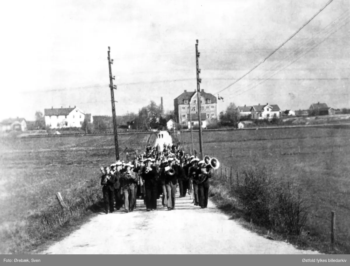 Frigjøringa feires med tog på Hauge, Rolvsøy i mai 1945. Musikkorps i front. Hauge skole i bakgrunnen.