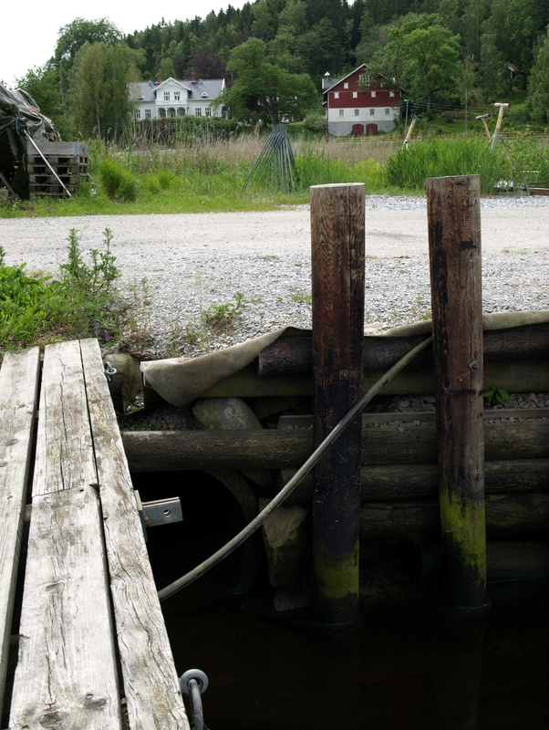 Fra sjøveien ser man inn mot Møla med mange brygger og småbåter. Sørover ligger en bondegård og et nyere boligfelt. Foto: Bodil Andersson, Østfoldmuseene-Halden historiske Samlinger.