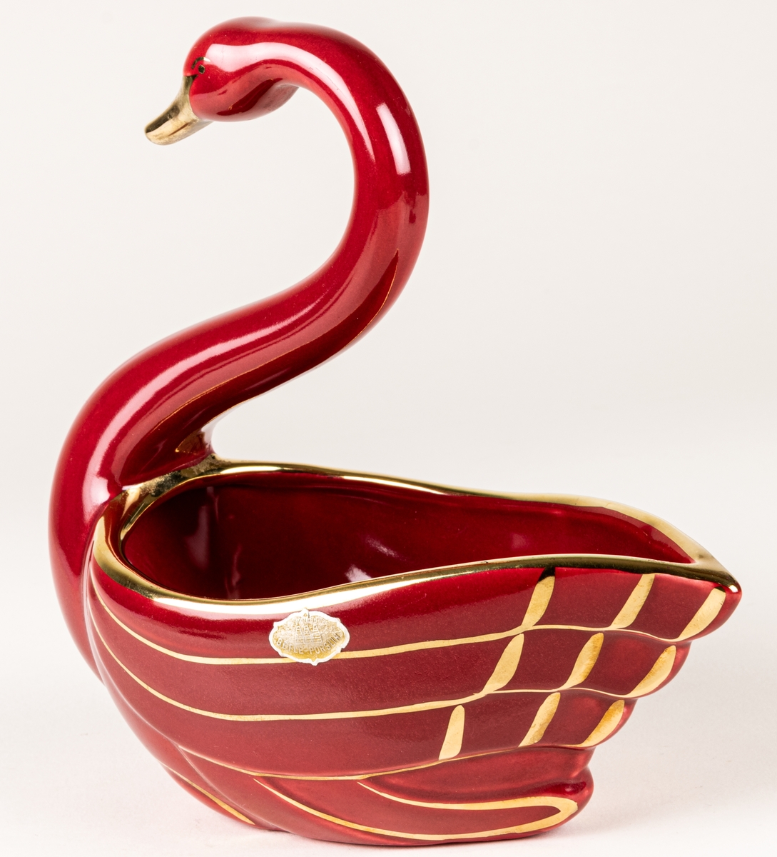 Prydnadsfigur eller skål i form av en svan, flintgods, modell A, dekorserie Rubin; röd glasyr med handmålat guld. Rubin producerades under åren 1940-1958. Oklart vem formgivaren är.