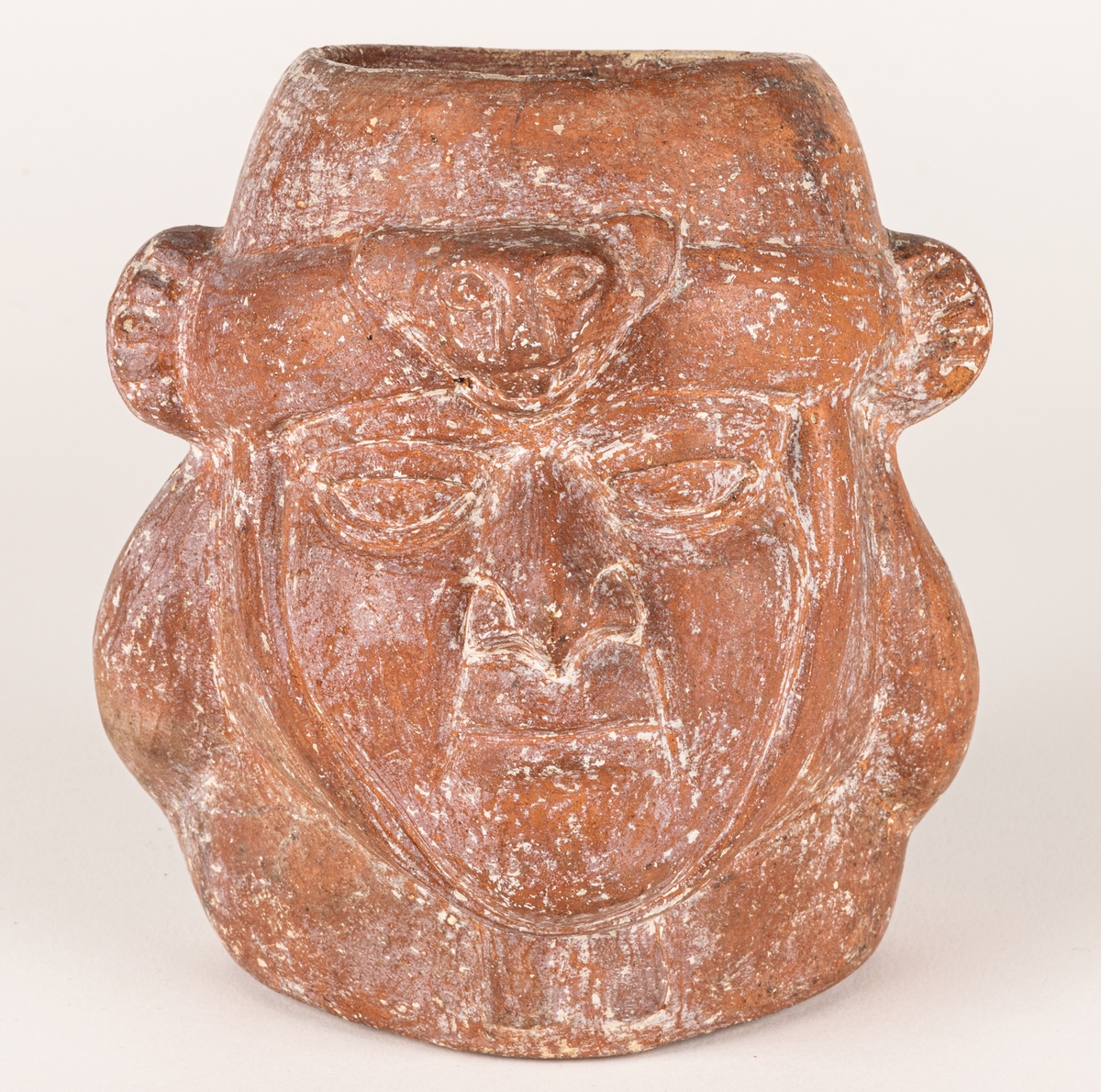Gravkärl, av rödbrun lera med kraftig relief i form av ett ansikte. Ova öppning upptil. Inkaiskt gravkärl.