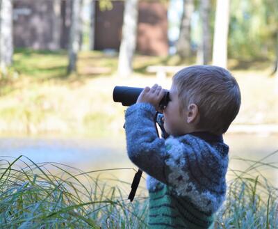 Foto av en gutt som ser i en kikkert ute i naturen