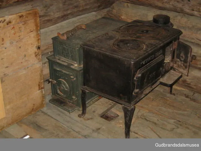 Vedfyrt komfyr i støpejern, modell no. 56, produsert av Kværner Brug på 1920-tallet. To kokeplater, ett varmerom samt oppgang for ovnsrør på ovnsplate. Komfyren har dører for ovn og brennkammer på front samt fire bein av støpejern.