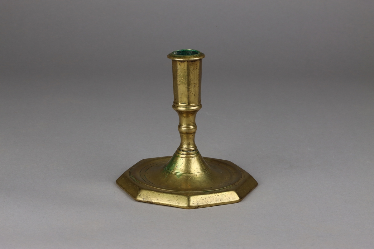 Octogonal brass candlestick with a moulded short baluster steam and a foot with sunken centre. The octogonal nozzle with mouldings at the top and bottom.