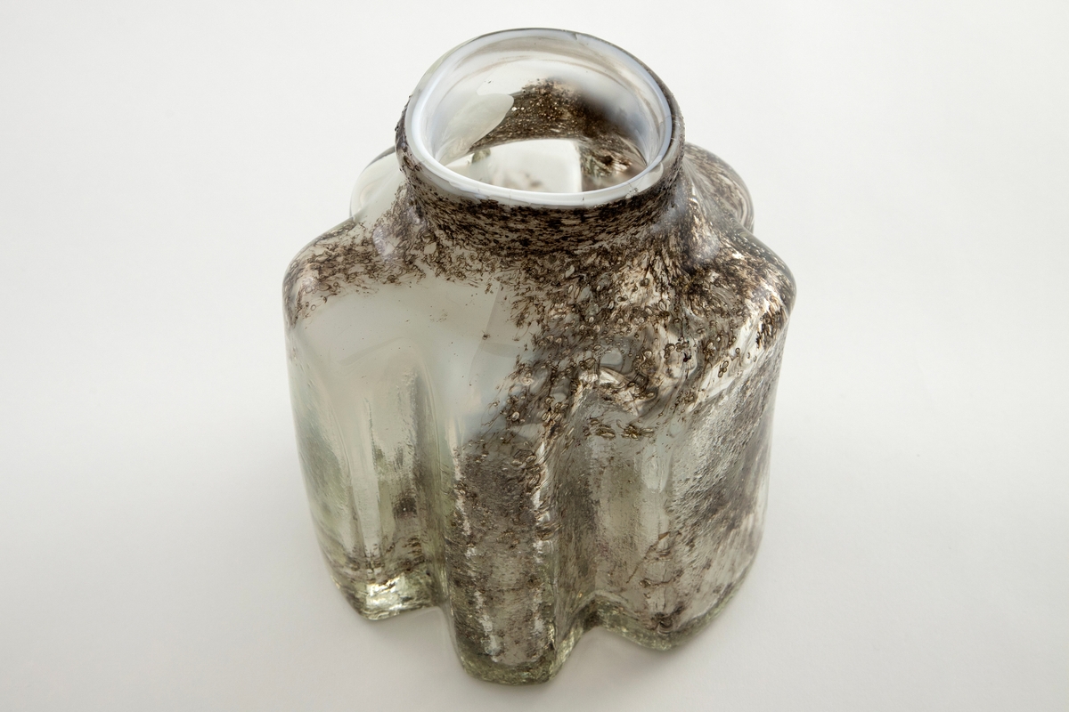 Vase av klart glass med melkehvite partier og innlagt metallfiberdekor. Vasen har rette vegger som er formet i irregulære bølger og en glatt hals med rund munning.