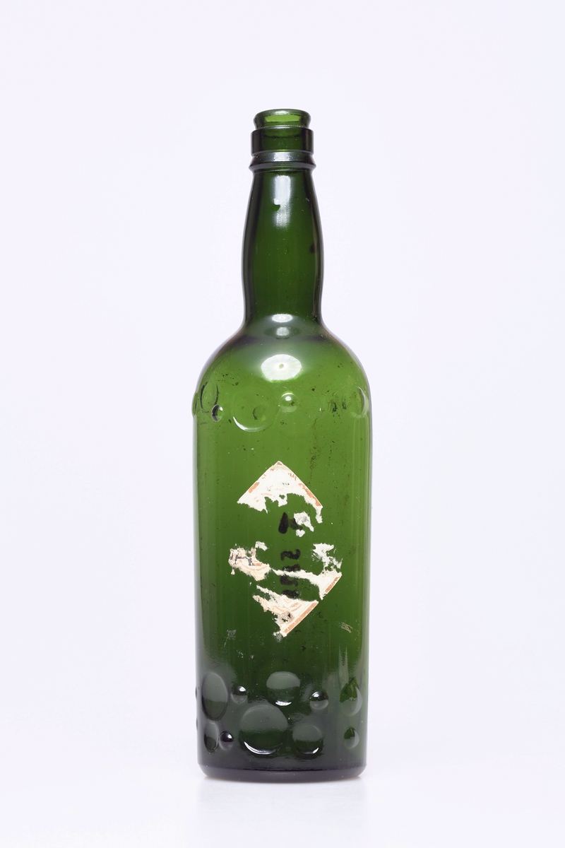 Grønt glass, fabrikklaget. Det er to rekker med påstøpte merker på flasken og rester etter merkelapper.