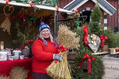Bildet viser en kvinne foran markedsboden sin som holder frem et julenek
