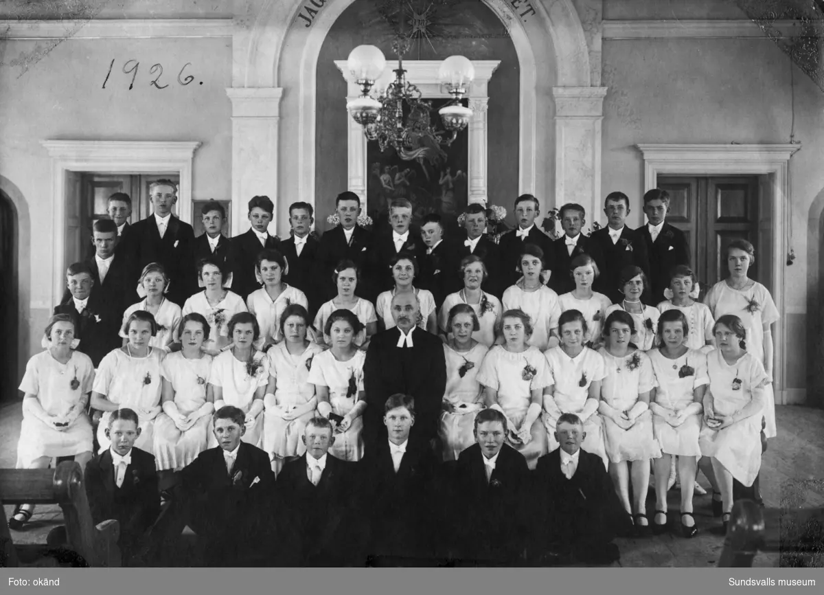 Gruppfoto med konfirmander och komminister L. J. Svedén i Heffners kyrkosal vid Malmtorget i Skönsberg, som låg där nuvarande (2022) Sundsvallsbrons norra brofäste är beläget. På bildens baksida står: Skönsberg 1926. Ur en samling från Skönsberg.