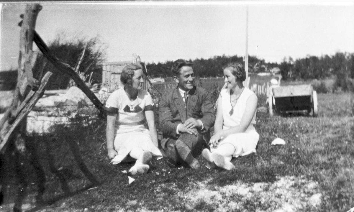 To kvinner og en mann sitter på et gårdstun.