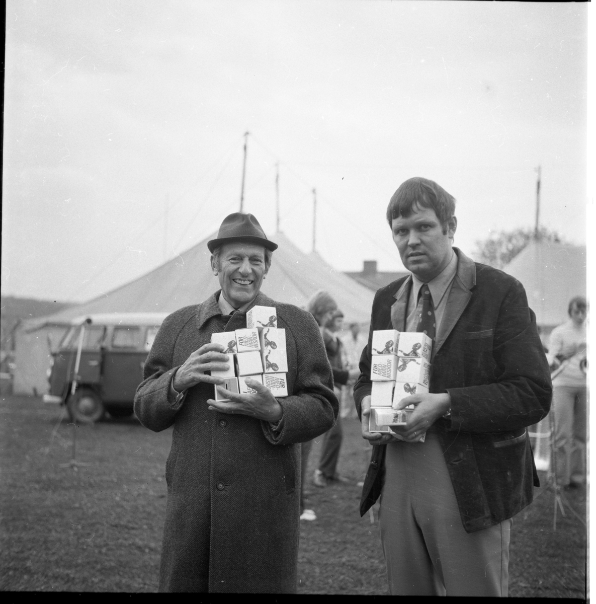 Två män framför ett stort tält. I famnen har de sannolikt sparbössor, märkta "För medmänniskor". Mannen till vänster är missionär Karl Ramstrand och till höger pastor Allan Wendefors.