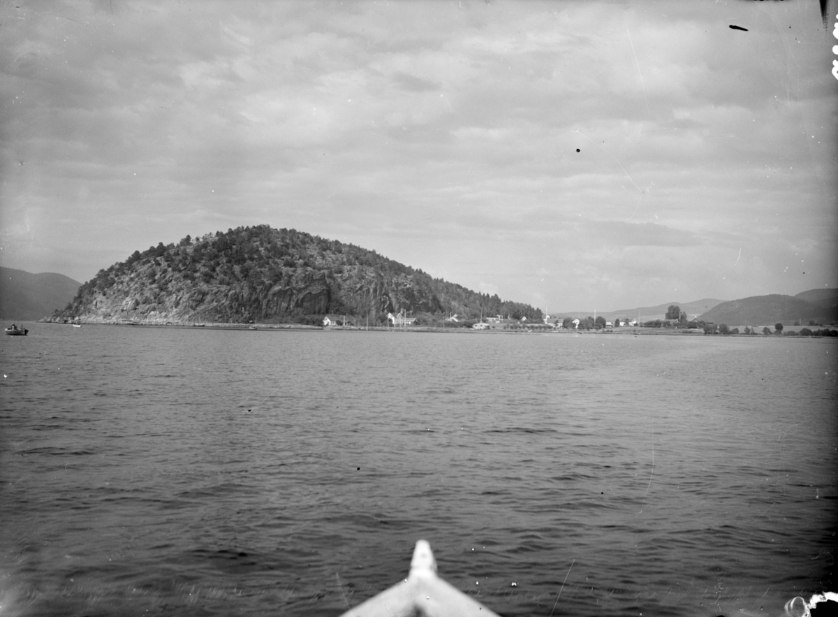 Landskapsfotografi fra en båt mot en bergkolle. Tekst fra Teigens katalog: "Svelviks Historie, Svelviks museum etc. se også: Drammens Tidende, se også: Hurum Bygdebok 4938"