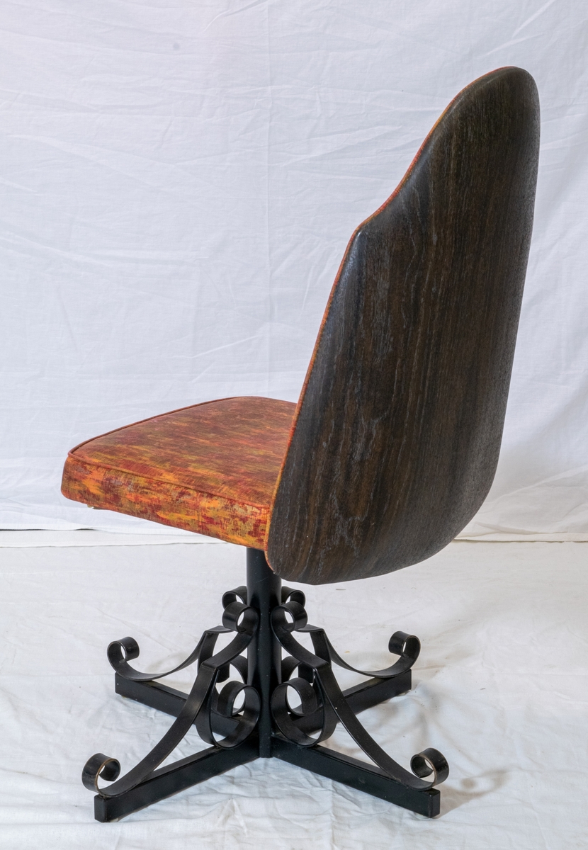 Spisestuestol med rødbrunt trekk. Bein i sort metall minner om smijern og bakplate i plast med tremønster.