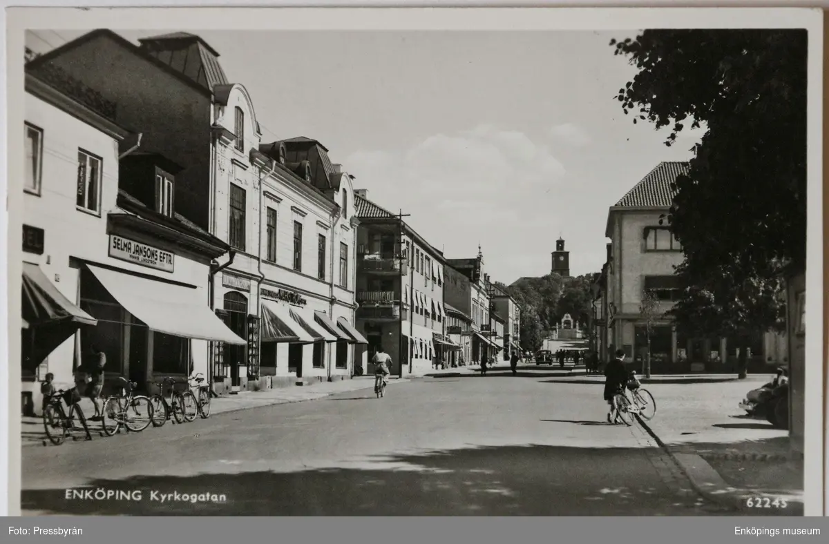 Vykort med motiv av Kyrkogatan, Enköping. Vy från Torget, till höger, upp mot Vårfrukyrkan. Fotat tidigast slutet av 1930-talet.