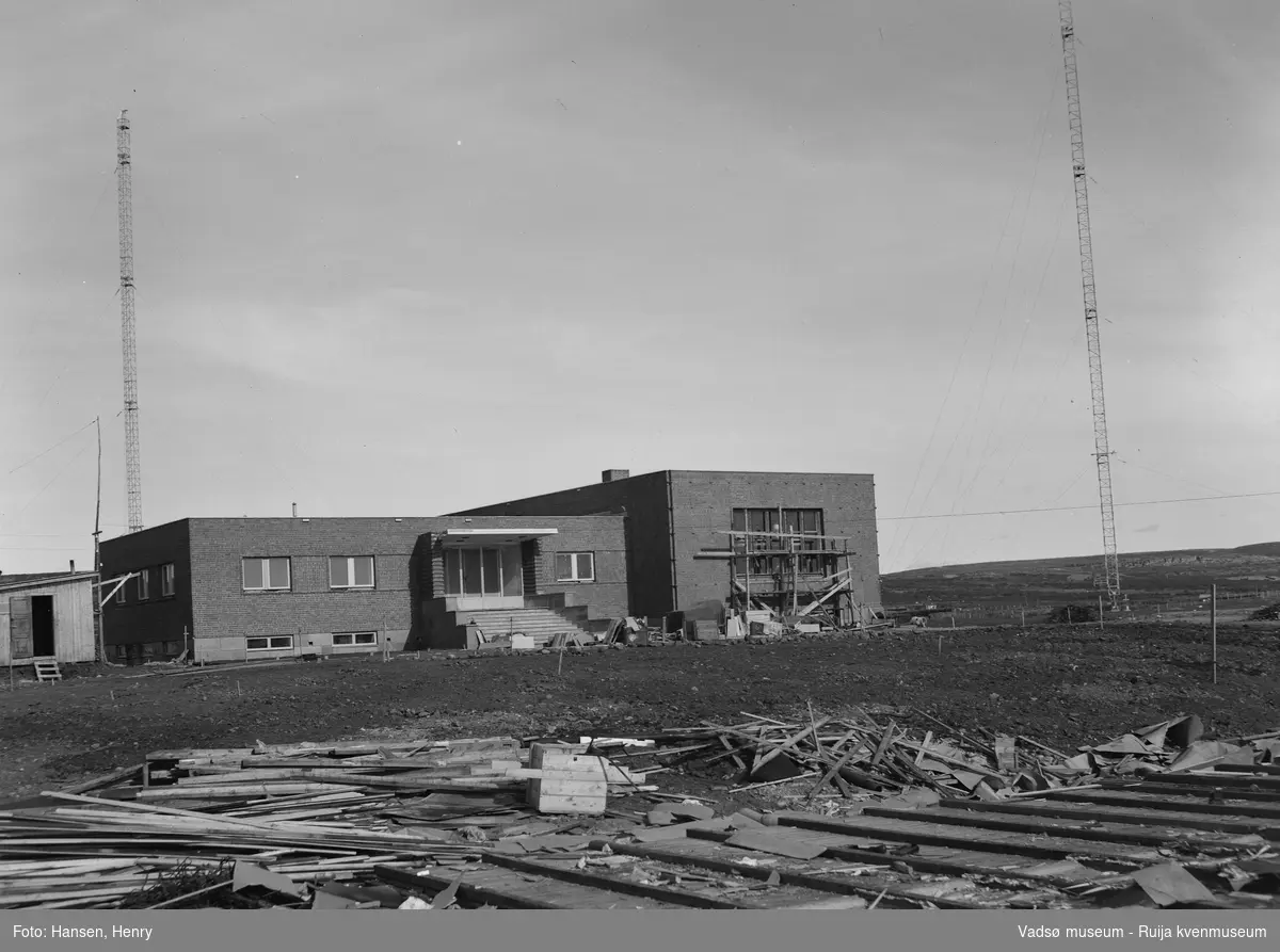 Det nye NRK-bygget i Vadsø ble reist 1948-49. Bildet er tatt mot nordøst. Bygningen er ennå ikke helt ferdigstilt og vi kan vi se stillaser,  forskalingsmateriale,  og arbeidsbrakke rundt bygningen. Vi ser også de to radiomastene.