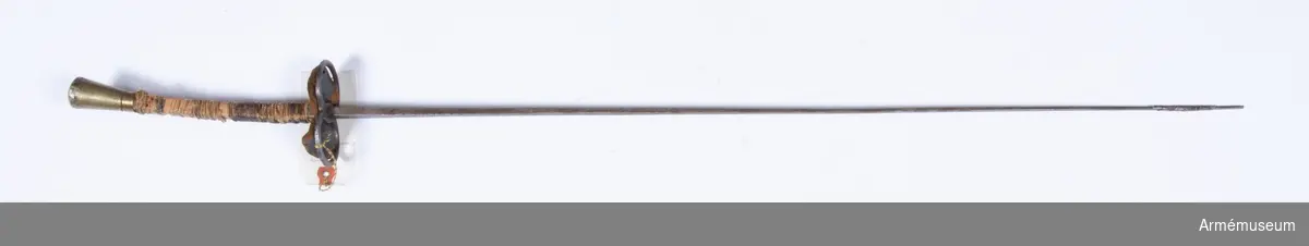Florett, Frankrike ca 1910.
Fäste med konisk, sliten knapp av mässing, fasad kant på ovansidan. Rektangulär, svagt böjd kavel av trä med närmast kvadratiskt tvärsnitt, till stora delar lös kavellindning av tunt lingarn omväxlande med tvinnad tråd. Nertill mässingsring fyrkantig som kaveln, övre kaveln.

Parerplåt i form av två ovala ringar av stål med läderskiva av samma form på ovansidan, undersidan svart.

Klinga med närmast kvadratiskt tvärsnitt, jämt avsmalnande mot spetsen. Spetsen avbruten och lagad med lindning av bly(?). På bredsidorna 40 mm från fästet stämplat: "EXCELSIOR  // MARQUE// DEPOSÈE" (Marque Deposèe på två rader med samma bredd som Excelsior) samt intill fästet på ena sidan stämpel: 4 och på den andra P.B(?).